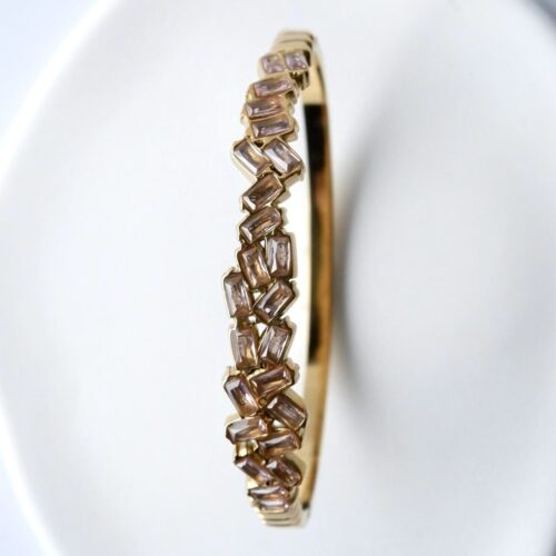 Gold Staggered Baguette Crystal Bangle on a plaster background