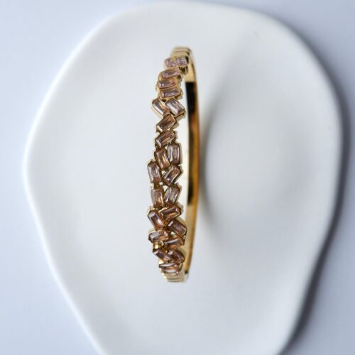 Gold Staggered Baguette Crystal Bangle on a plaster background